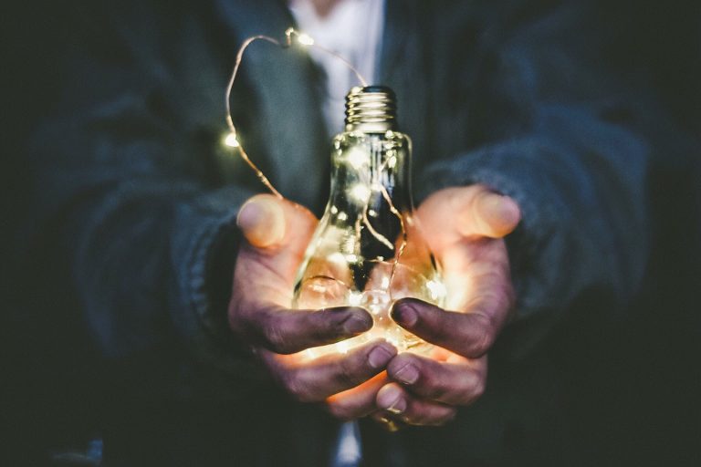 Close-up of hands holding a glowing light bulb wrapped in string lights, symbolizing bright ideas, creativity, and strategic branding solutions.