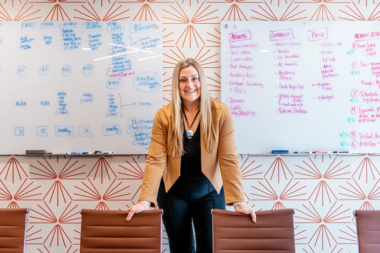 Smiling businesswoman standing in a modern conference room with whiteboards covered in marketing strategy notes, symbolizing planning, organization, and professional growth.