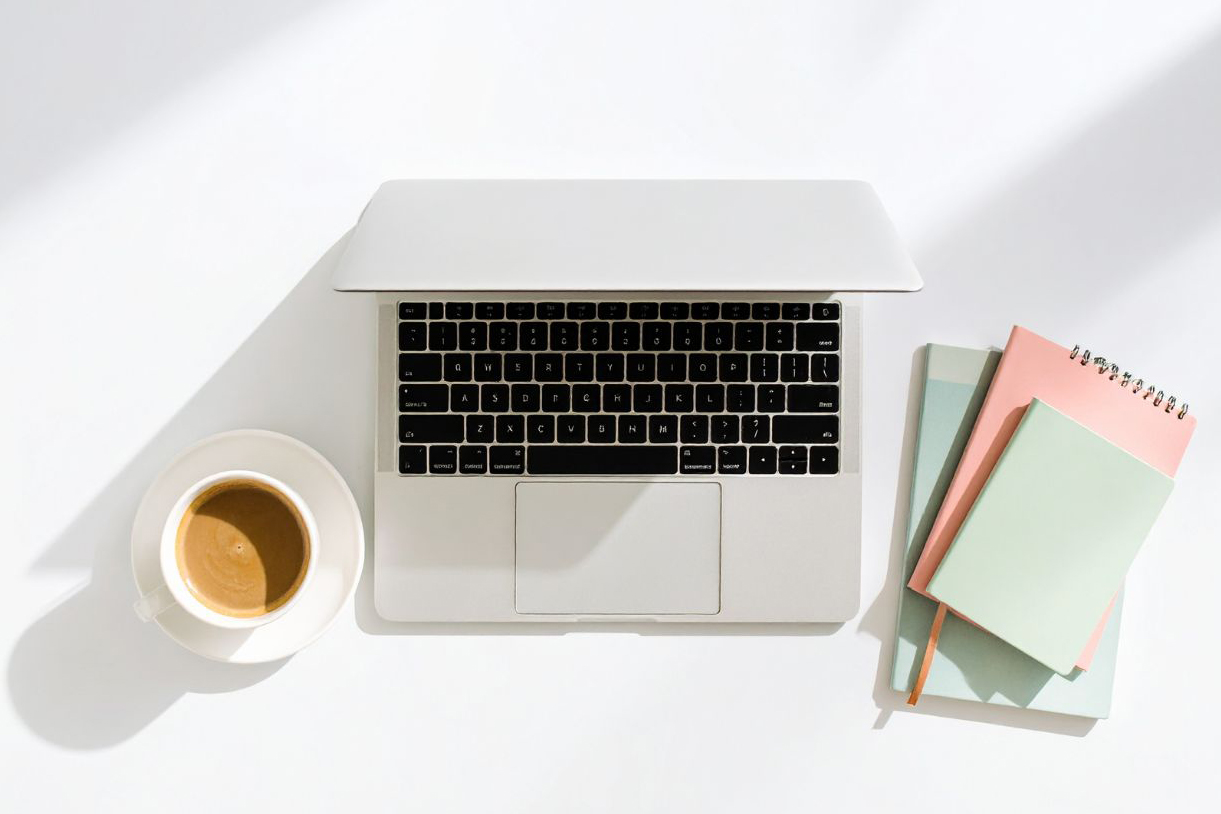 Minimal workspace with laptop, coffee, and pastel notebooks symbolizing creative brand strategy and thoughtful naming process.